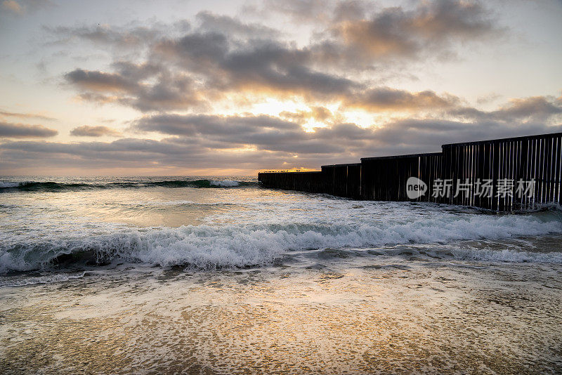 海滩和海浪的近景日落附近的国际边界墙在Playas Tijuana，墨西哥